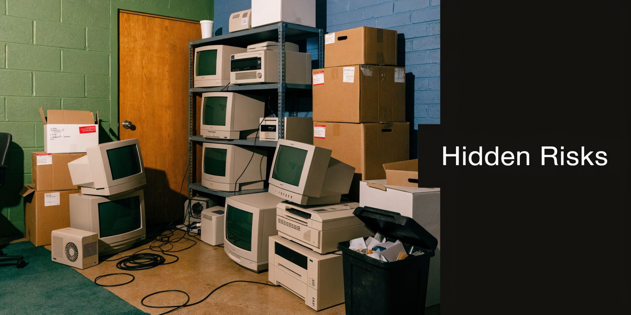A cluttered room containing piles of old cathode ray tube computer monitors, printers, and cardboard boxes.