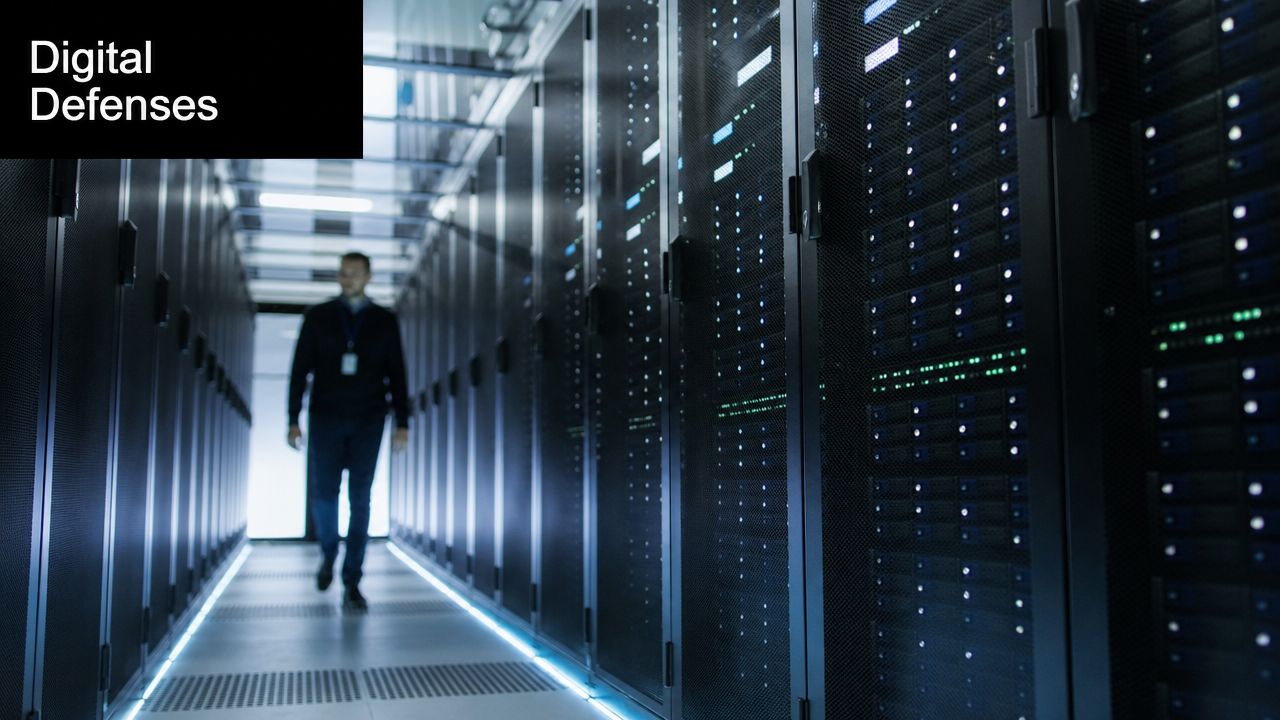 A technician walking down a corridor in a modern high-security server room data center.